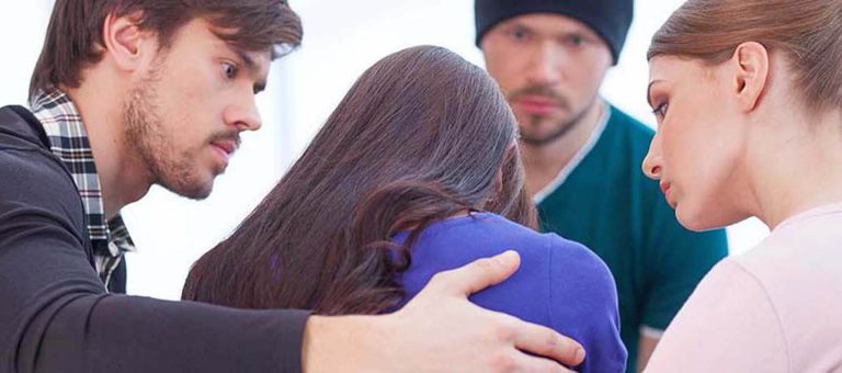 Group of people sitting closely together offering emotional support to a woman in distress.