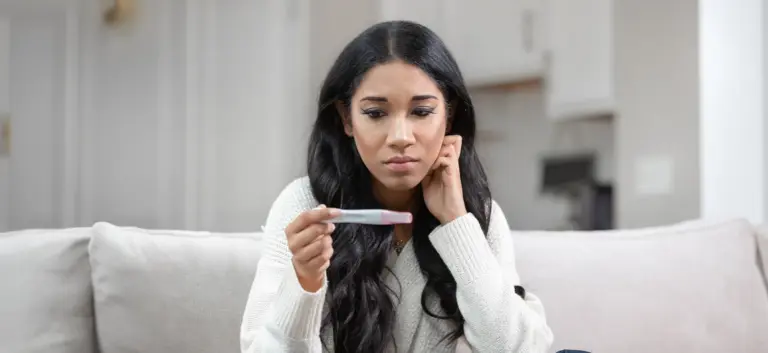 Young woman sitting on a couch looking at a pregnancy test with concern.